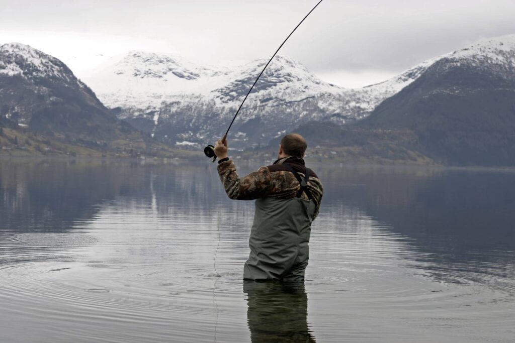 man fly fishing on a lake with snow capped mountains in the back ground